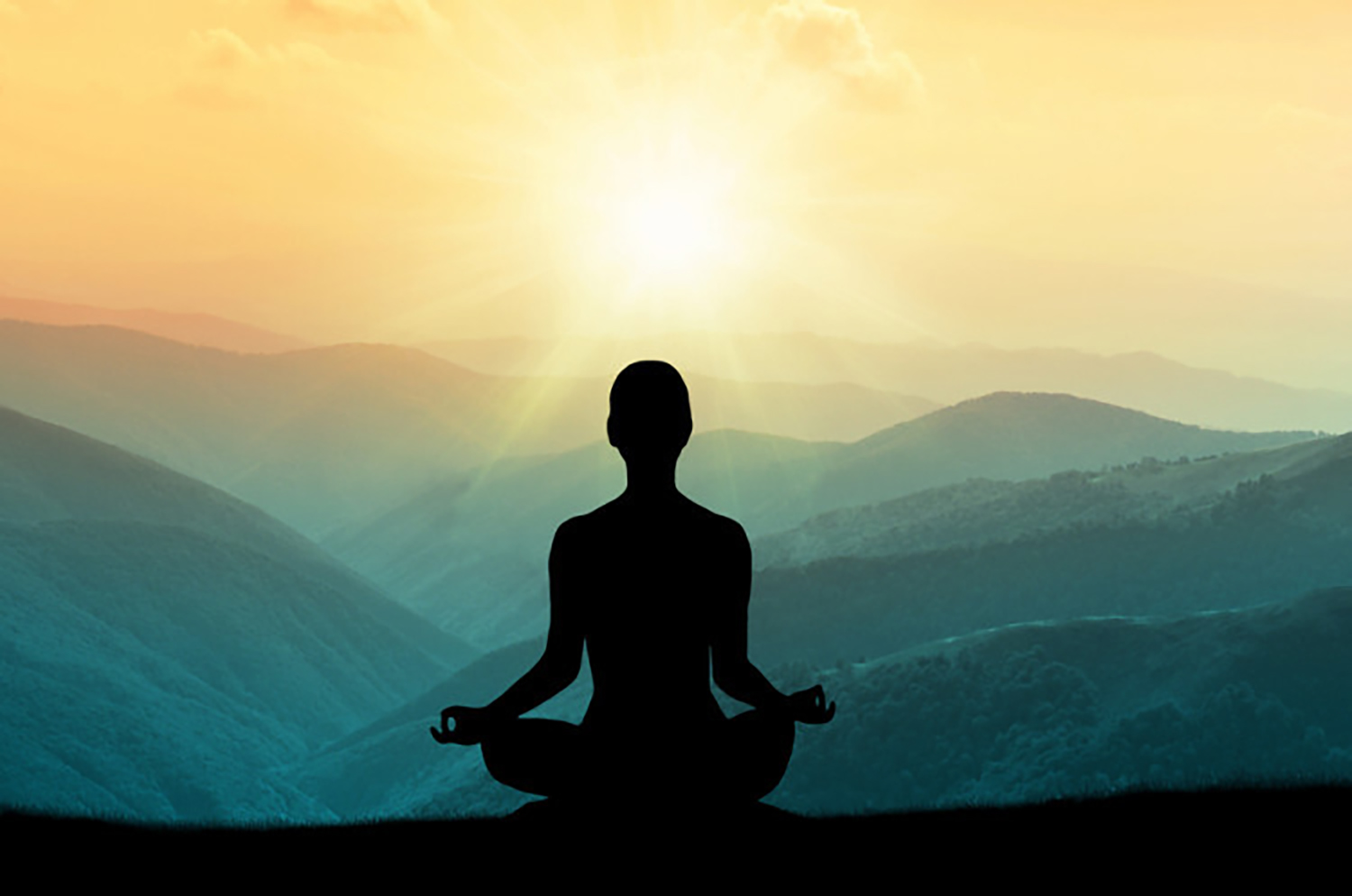 A person meditating on a hilltop as the sun rises over the mountains